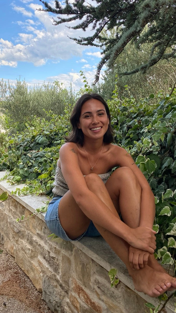 Angela, founder of Boosh, sitting on a stone wall and smiling